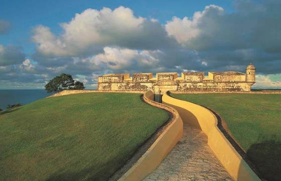 The fortified walls of Campeche at sunset, with a yellow walkway leading toward the sea and colonial ramparts. 