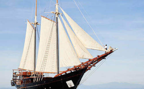The elegant Amandira yacht sailing on calm Indonesian waters under a clear blue sky, showcasing its traditional twin-mast design. 