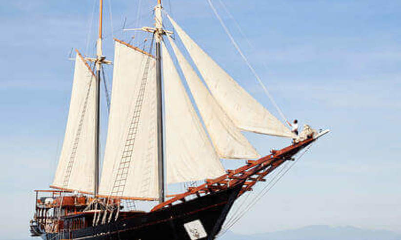 The elegant Amandira yacht sailing on calm Indonesian waters under a clear blue sky, showcasing its traditional twin-mast design. 