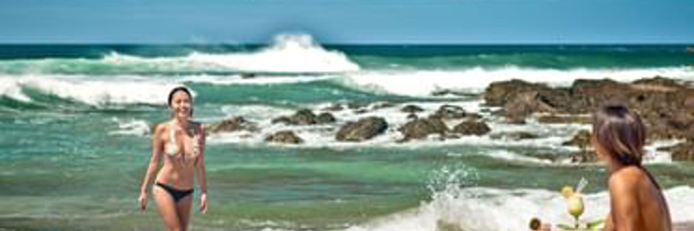 A couple enjoys a sunny day on the beach, with turquoise waves rolling in a long Costa Rica's Pacific coast. 