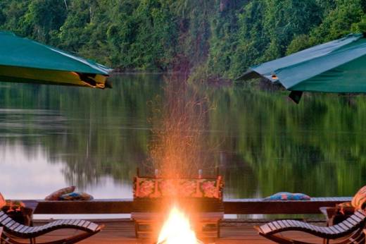 Floating deck with firepit and umbrellas at Cristalino Jungle Lodge, overlooking a tranquil river at sunset in Brazil. 