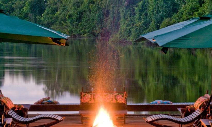 Floating deck with firepit and umbrellas at Cristalino Jungle Lodge, overlooking a tranquil river at sunset in Brazil. 