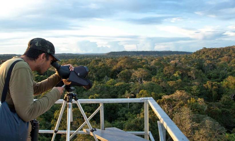 Birdwatcher using a spotting scope on canopy tower overlooking Amazon rainforest at Cristalino Jungle Lodge in Brazil. 