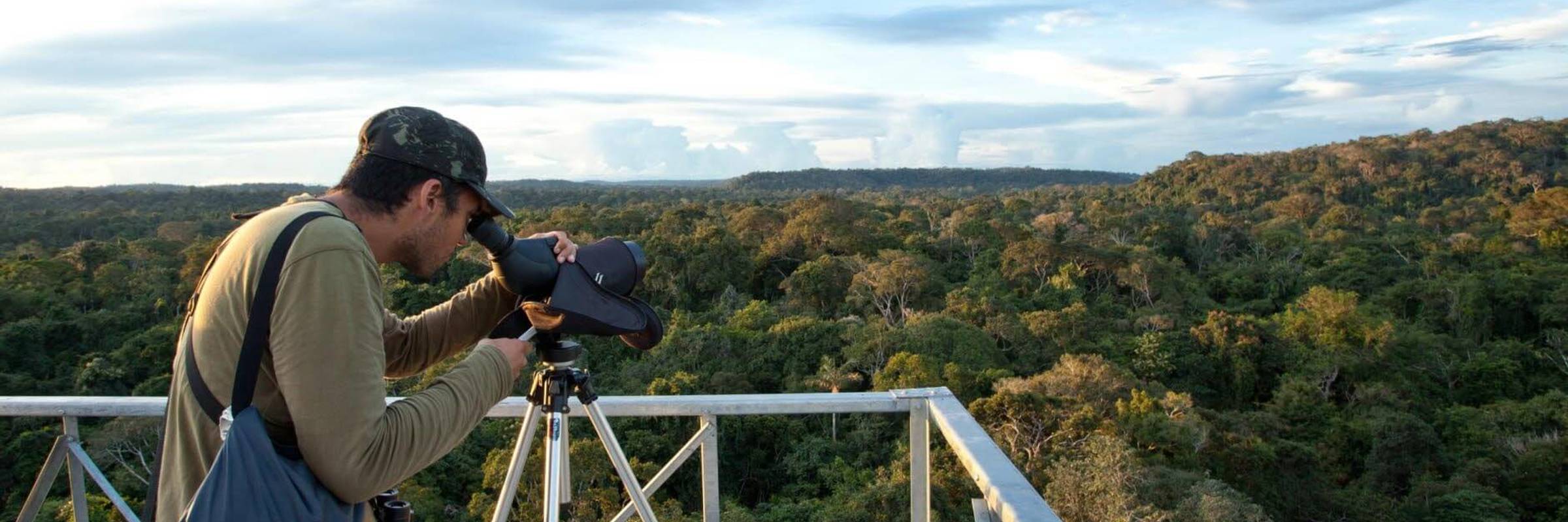 Birdwatcher using a spotting scope on canopy tower overlooking Amazon rainforest at Cristalino Jungle Lodge in Brazil. 