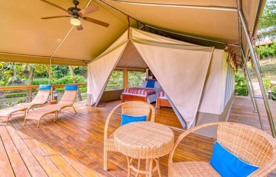 A spacious glamping tent with cozy furnishings and wooden deck invites relaxation amid the natural beauty of Costa Rica. 