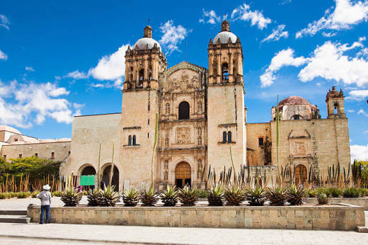 Santo Domingo Church in Oaxaca, Mexico, with its twin bell towers and historic Baroque facade under a blue sky. 