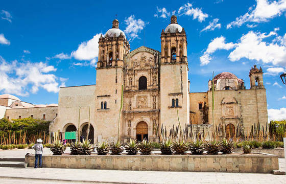 Santo Domingo Church in Oaxaca, Mexico, with its twin bell towers and historic Baroque facade under a blue sky. 