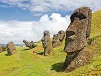 Iconic Moai statues of Easter Island stand on grassy hills under a dramatic sky at Rano Raraku quarry. 