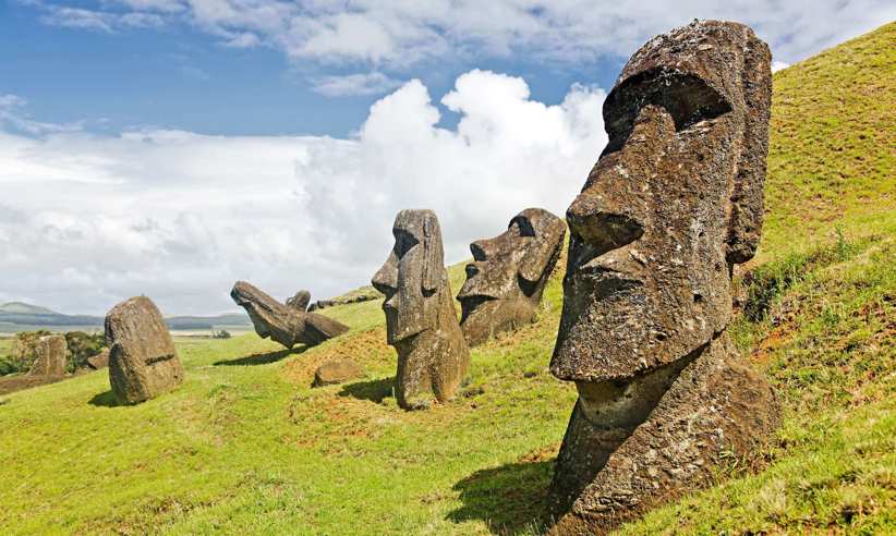 Iconic Moai statues of Easter Island stand on grassy hills under a dramatic sky at Rano Raraku quarry. 