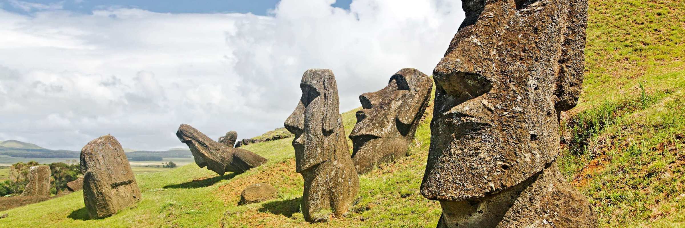 Iconic Moai statues of Easter Island stand on grassy hills under a dramatic sky at Rano Raraku quarry. 