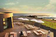 Outdoor terrace at Nayara Easter Island overlooks the ocean at sunset with tables, parasols, and scenic views. 