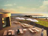 Outdoor terrace at Nayara Easter Island overlooks the ocean at sunset with tables, parasols, and scenic views. 