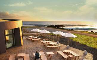 Outdoor terrace at Nayara Easter Island overlooks the ocean at sunset with tables, parasols, and scenic views. 