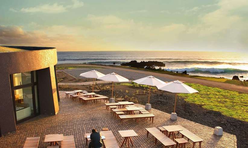 Outdoor terrace at Nayara Easter Island overlooks the ocean at sunset with tables, parasols, and scenic views. 