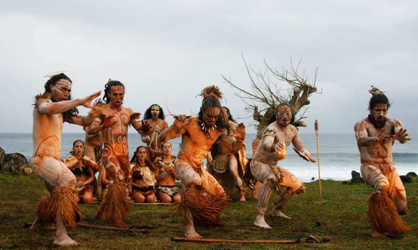 Traditional Rapa Nui dancers in costume perform on Easter Island with ocean backdrop and cultural heritage on display. 