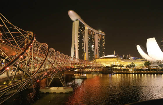 Night view of Marina Bay Sands and the illuminated Helix Bridge reflecting on the water in Singapore. 