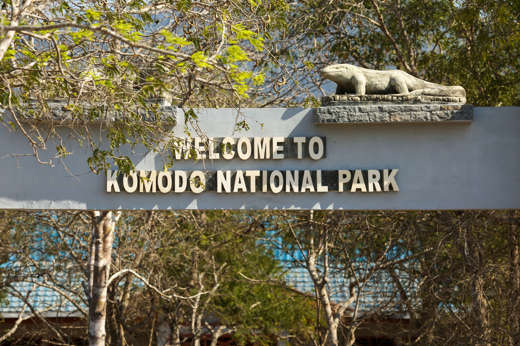 Entrance sign to Komodo National Park in Indonesia, featuring a carved Komodo dragon statue and shaded by forest trees. 