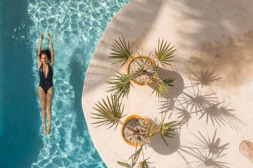 Overhead view of the swimming pool at Casa Sandra on Holbox Island, with tropical plants and a guest swimming below. 