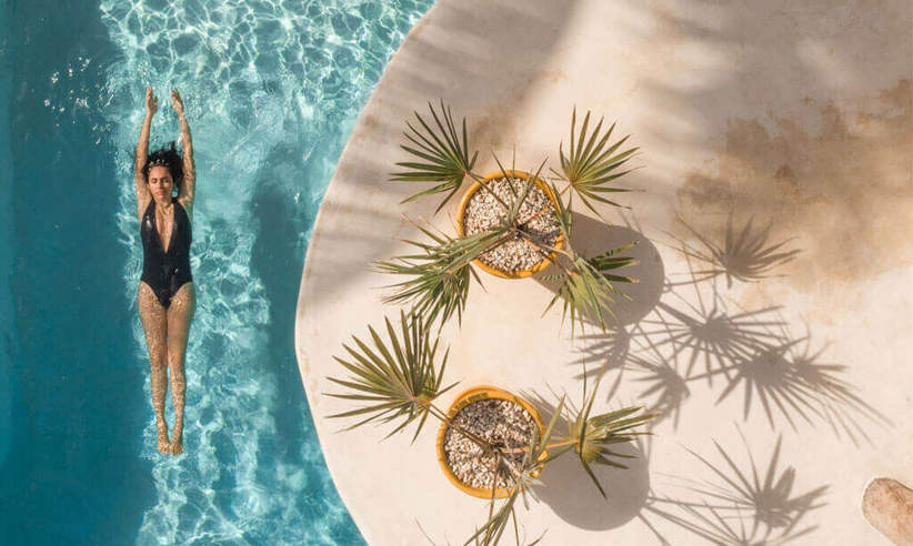 Overhead view of the swimming pool at Casa Sandra on Holbox Island, with tropical plants and a guest swimming below. 