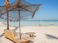Beachfront daybeds and thatched parasol at Nomade Hotel Holbox with white sand and clear blue sea views. 