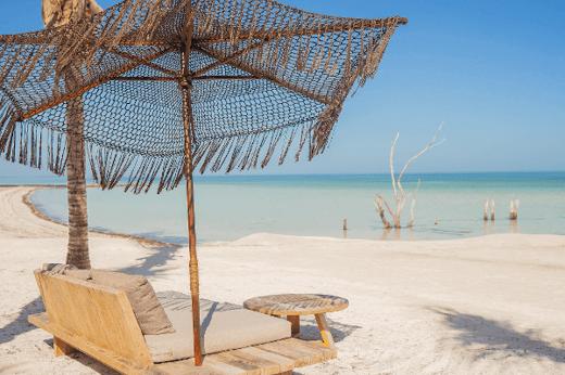 Beachfront daybeds and thatched parasol at Nomade Hotel Holbox with white sand and clear blue sea views. 