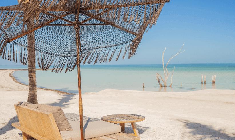 Beachfront daybeds and thatched parasol at Nomade Hotel Holbox with white sand and clear blue sea views. 