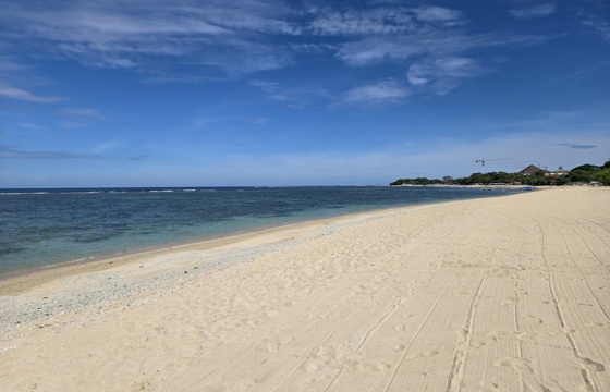 Tranquil white sand beach at Sanur, Bali with calm blue waters and a clear sky stretching along the coastline. 