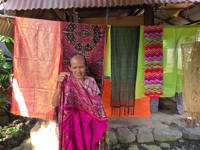 Elderly Indonesian woman showing vibrant handwoven textiles. 