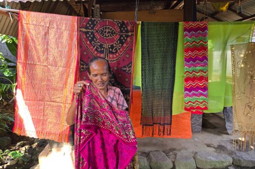Elderly Indonesian woman showing vibrant handwoven textiles. 