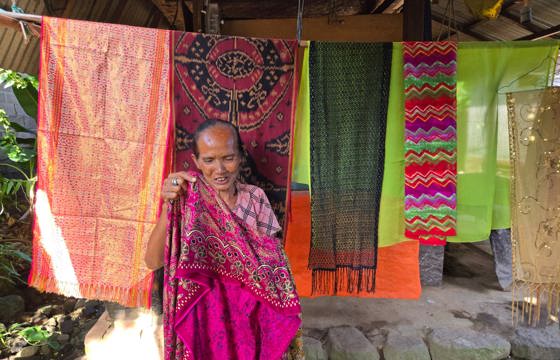 Elderly Indonesian woman showing vibrant handwoven textiles. 