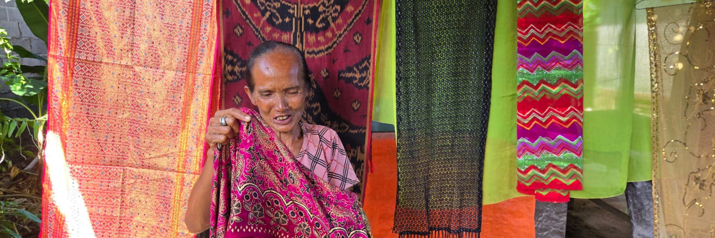 Elderly Indonesian woman showing vibrant handwoven textiles. 