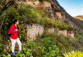 A hiker in a red jacket explores the ancient Kuelap Fortress ruins nestled in the mountains of Chachapoyas, Peru. 