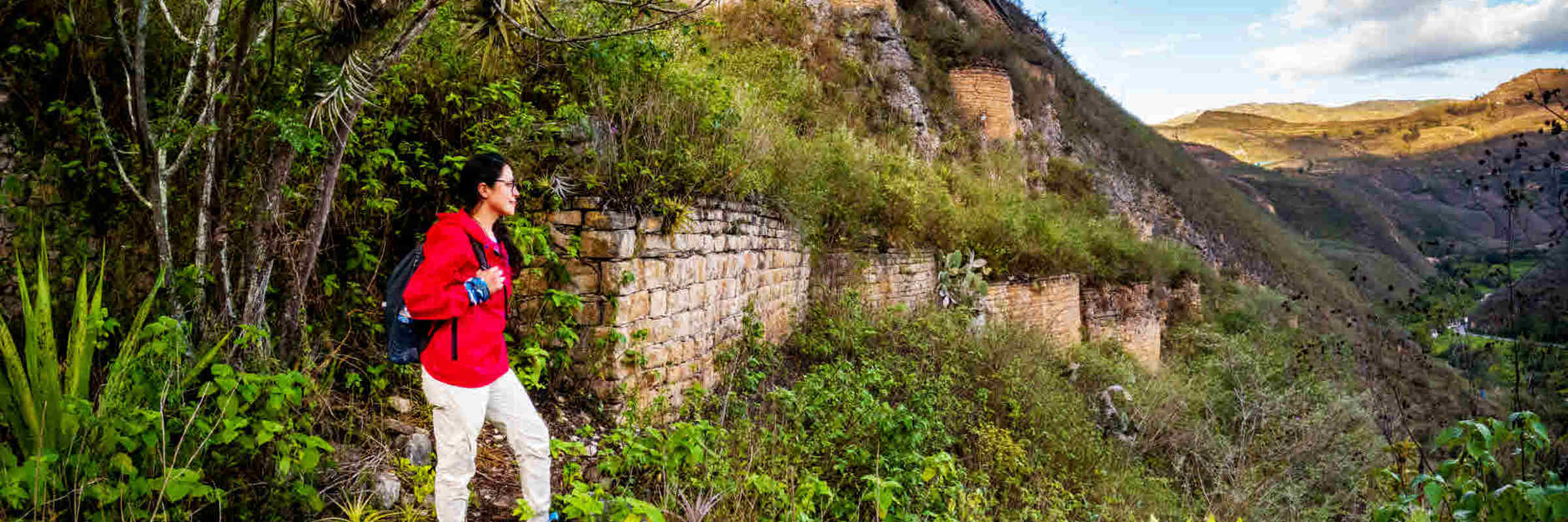 A hiker in a red jacket explores the ancient Kuelap Fortress ruins nestled in the mountains of Chachapoyas, Peru. 