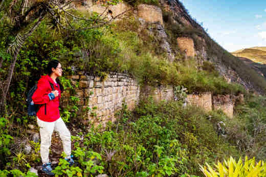 A hiker in a red jacket explores the ancient Kuelap Fortress ruins nestled in the mountains of Chachapoyas, Peru. 