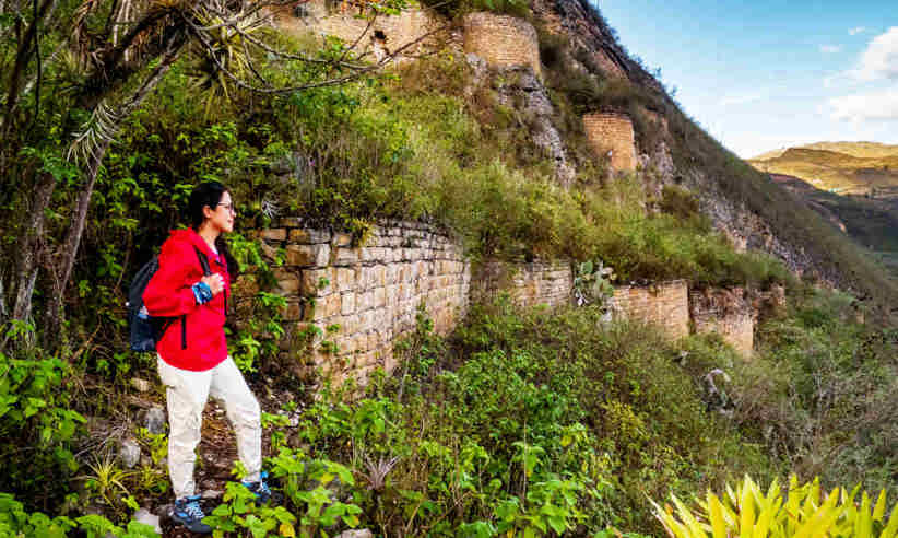 A hiker in a red jacket explores the ancient Kuelap Fortress ruins nestled in the mountains of Chachapoyas, Peru. 