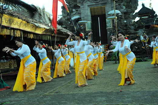 Balinese women in yellow sarongs performing a traditional temple dance during a ceremonial procession in Indonesia. 