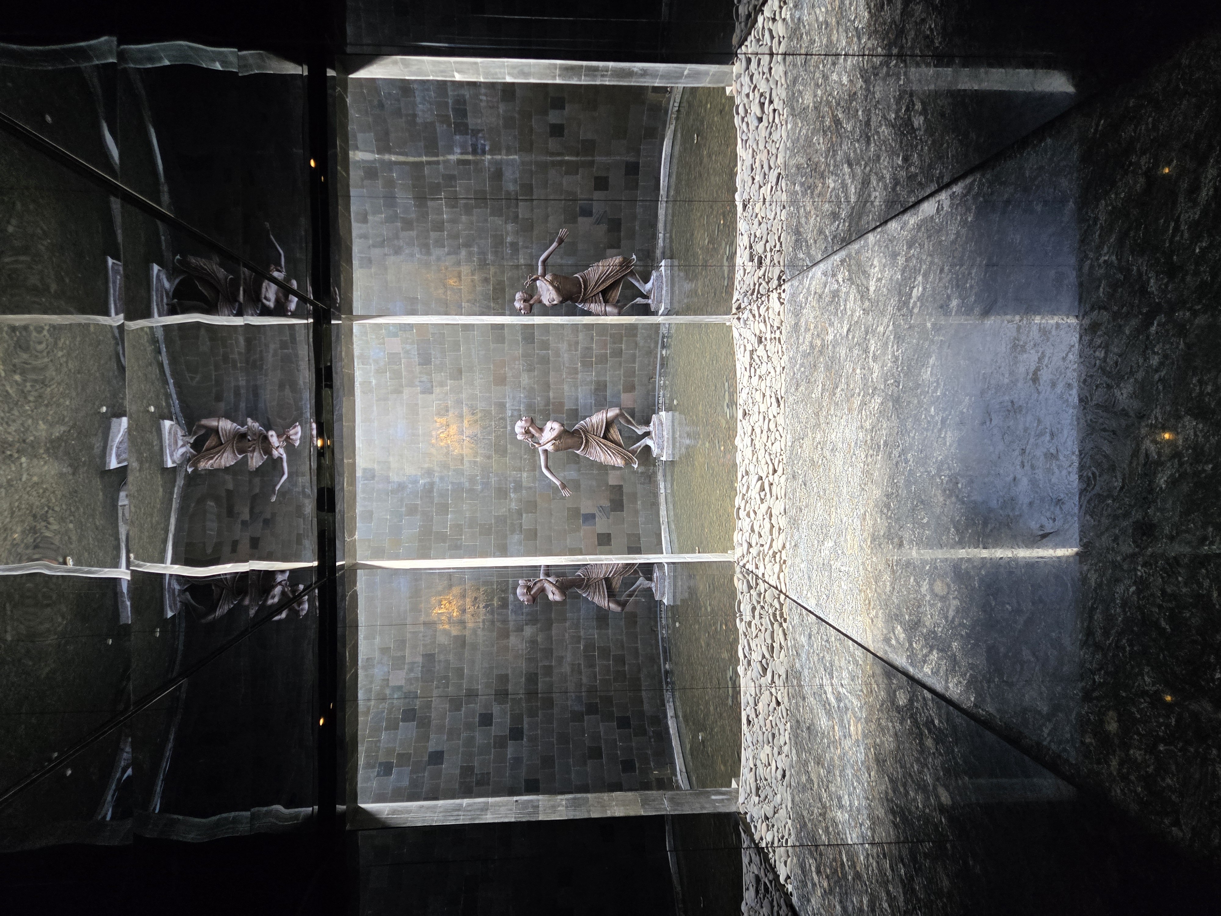 Modern spa interior in Bali with stone walls, statues, and reflect water features creating a tranquil ambiance. 
