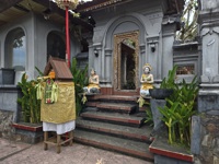 Ornate entrance to a Balinese temple, flanked by statues and an offering shrine, surrounded by tropical greenery. 