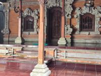 An ornate Balinese temple entrance with intricate stone carvings and wooden doors, set above a tiled platform in Indonesia. 