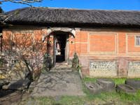 A traditional Balinese home entrance with stone path, red brick walls, and a thatched roof under a clear blue sky in Indonesia.