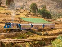Expedition train traveling through the Sacred Valley with golden fields and Andean mountains in the background. 