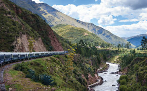 The Belmond Andean Explorer winds through a lush Andean valley beside a mountain river.