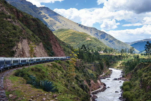 The Belmond Andean Explorer winds through a lush Andean valley beside a mountain river.