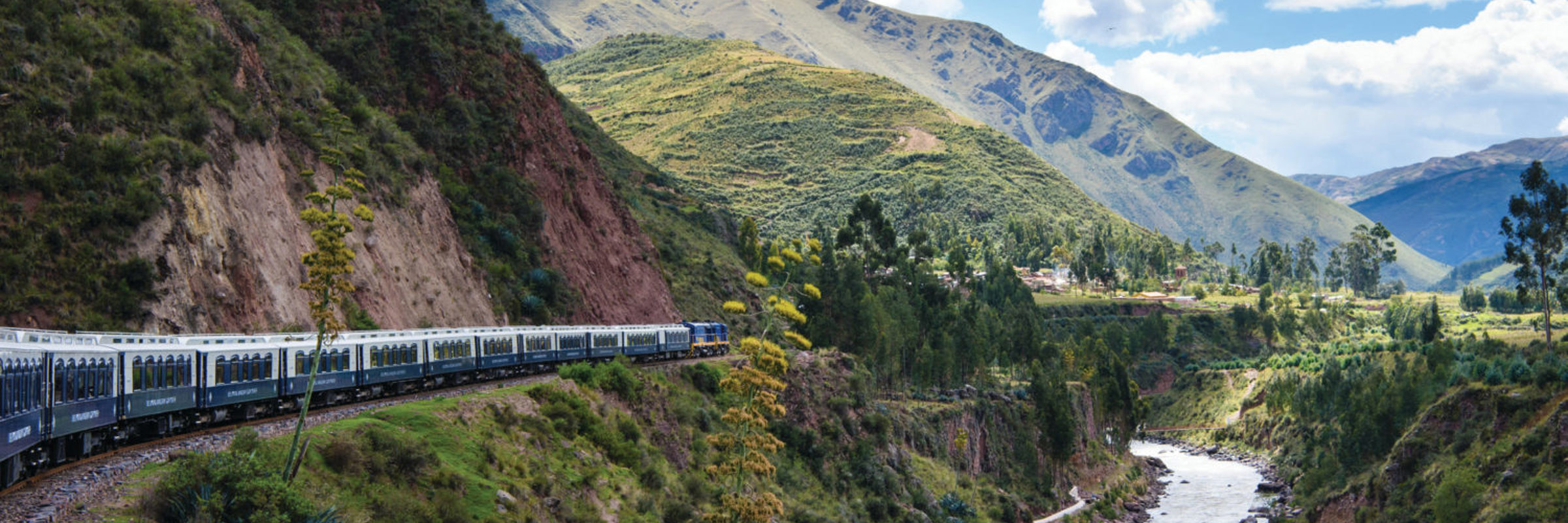 The Belmond Andean Explorer winds through a lush Andean valley beside a mountain river.