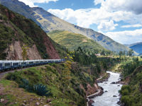 The Belmond Andean Explorer winds through a lush Andean valley beside a mountain river.