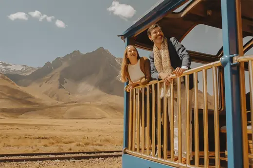 A couple takes in the panoramic mountain scenery from the observation deck of the PeruRail Titicaca Train. 