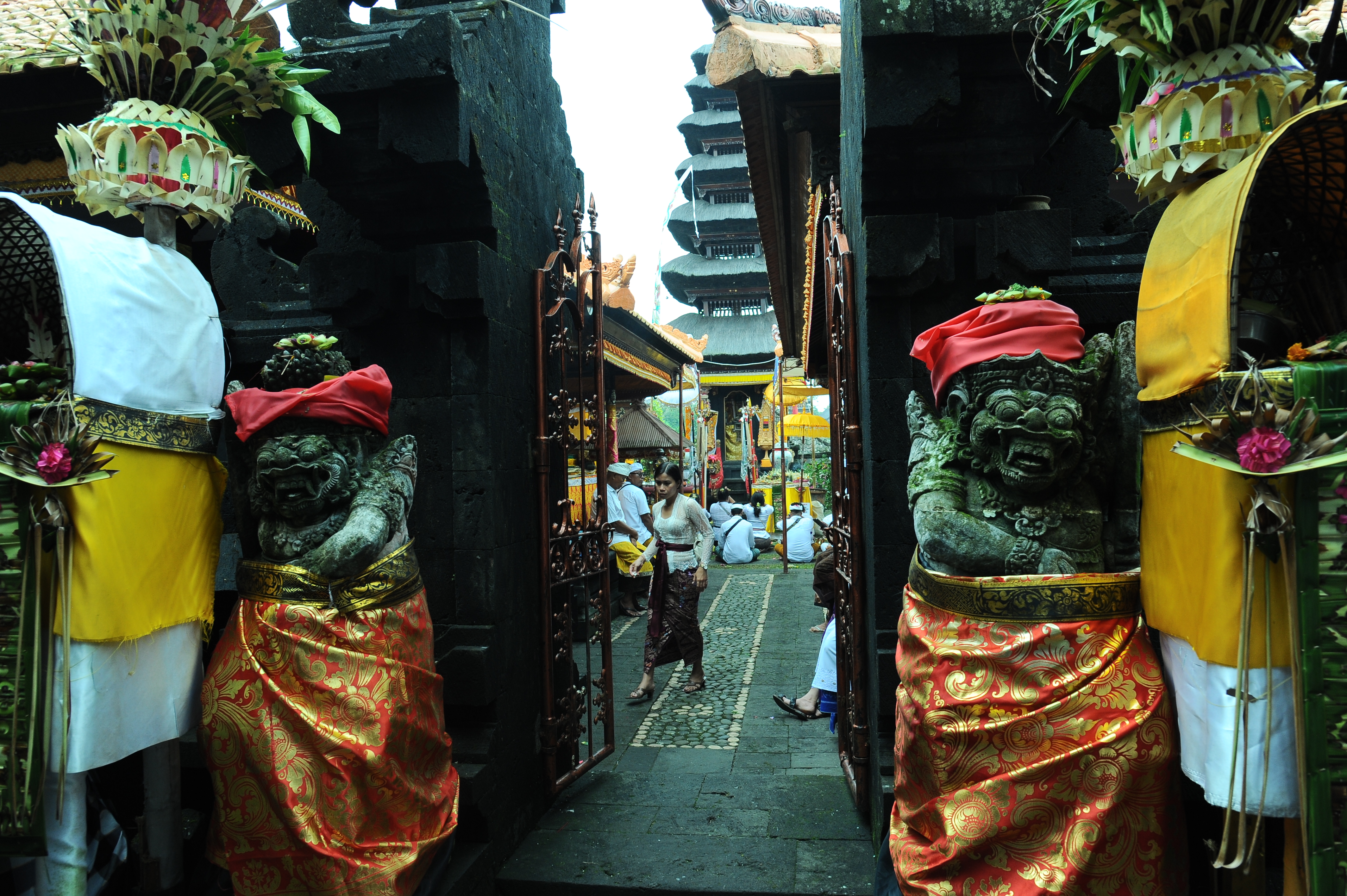 Traditional entrance to Besakih Temple in Bali, decorated statues and worshippers in ceremonial dress during temple rituals. 