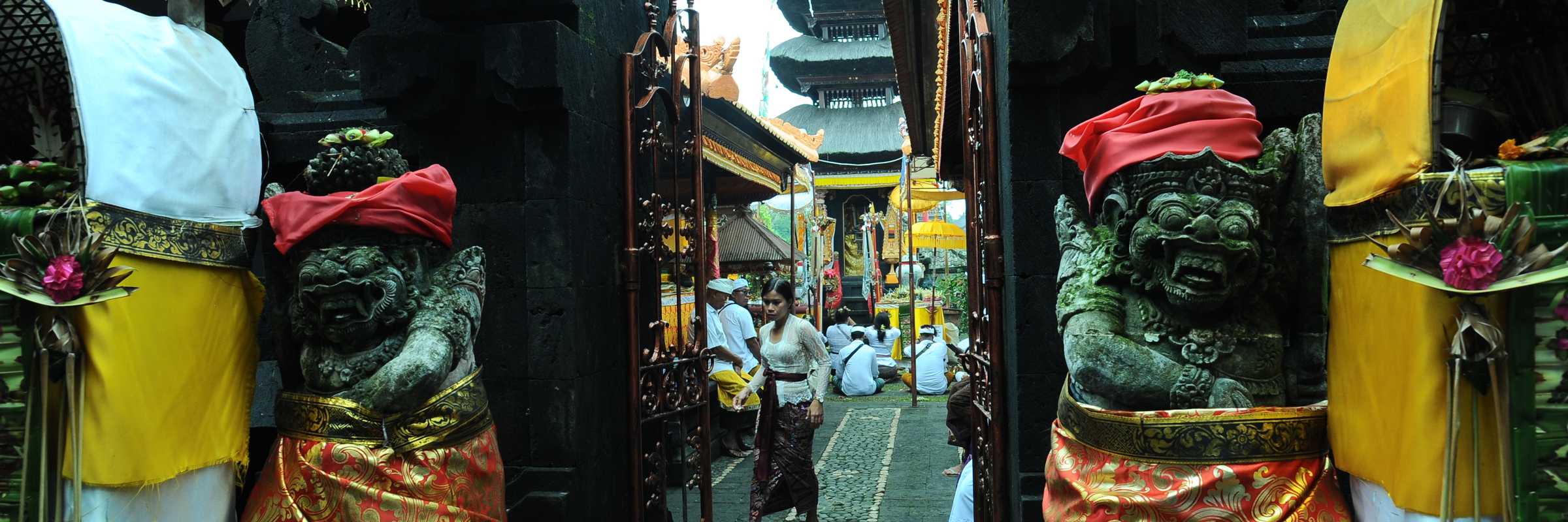 Traditional entrance to Besakih Temple in Bali, decorated statues and worshippers in ceremonial dress during temple rituals. 