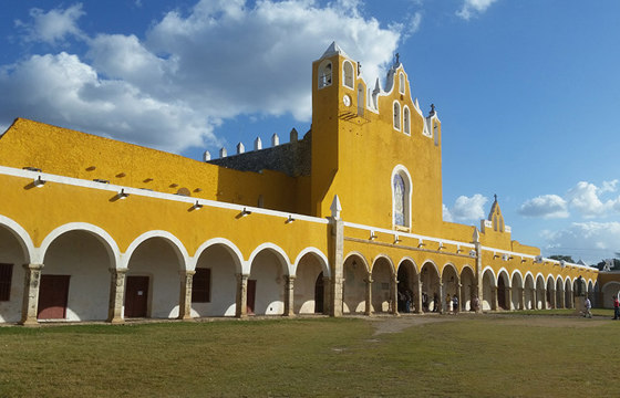 The iconic yellow Franciscan convent in Izamal, Yucatan, with its arched corridors and colonial architecture under blue skies. 