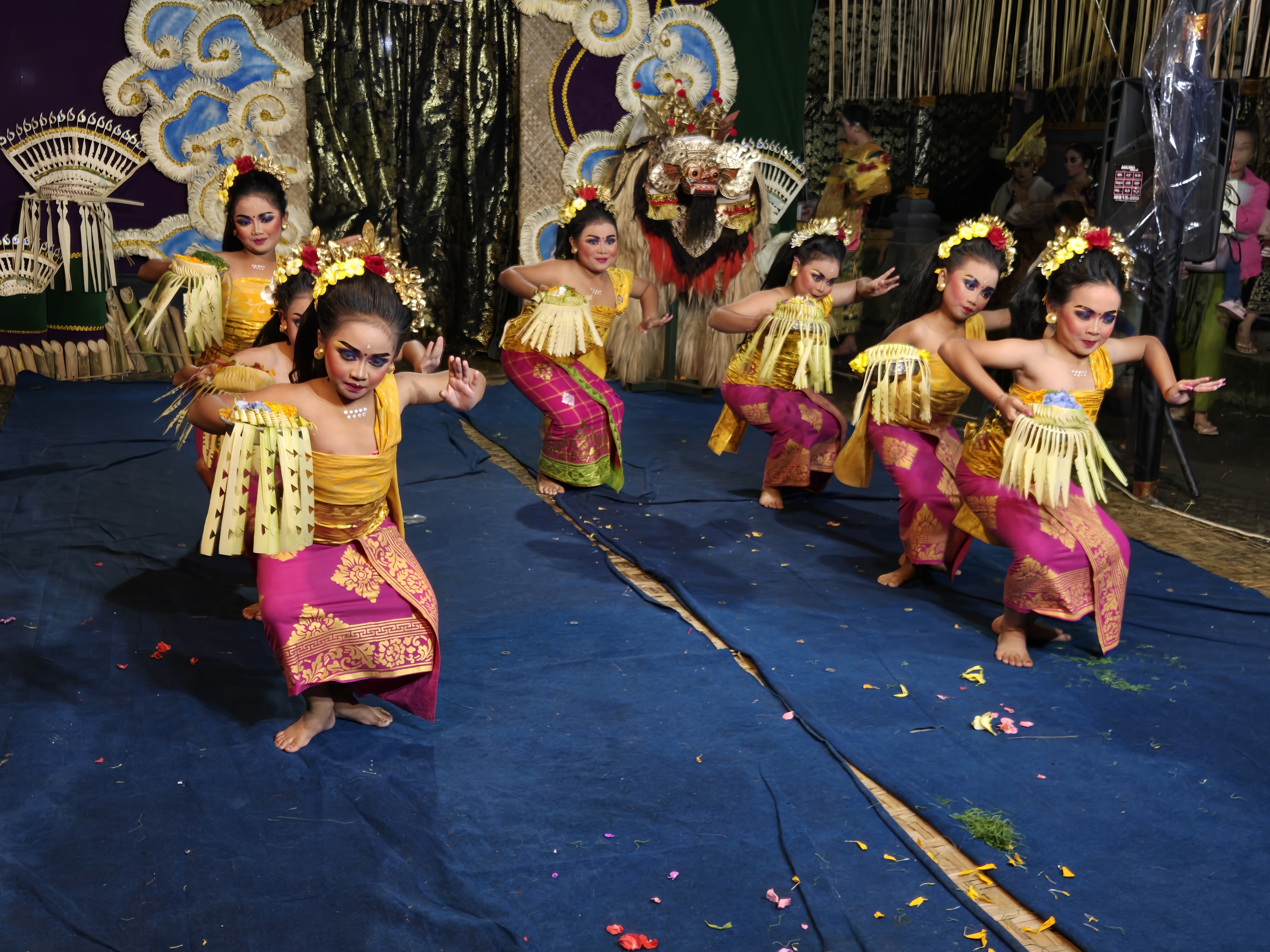Balinese girls in ornate costumes perform a synchronized traditional dance on stage, rich in colour, energy, and cultural flair. 
